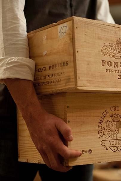 A Domaine employee carries wooden crates of wine in the process of wine organization for a collector's cellar.