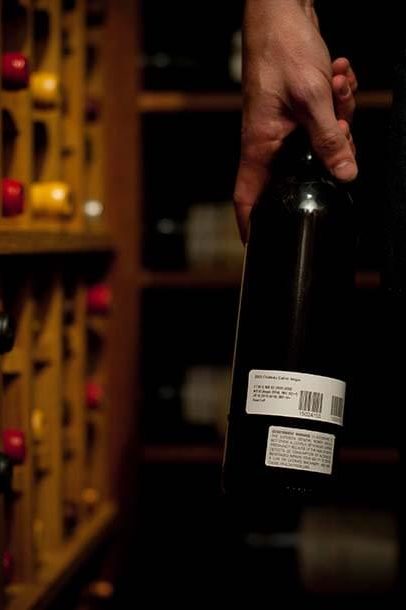 A hand holds a bottle of wine in a cellar that has been treated with professional wine organization from Domaine.