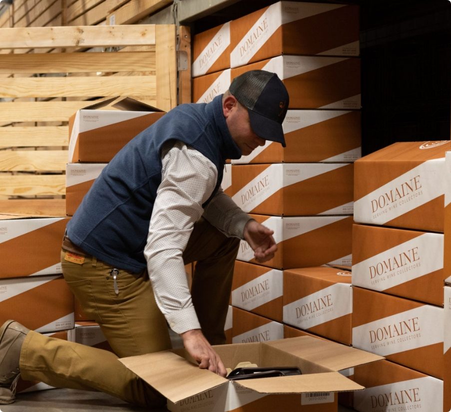 A Domaine employee packs bottles into boxes for wine storage.