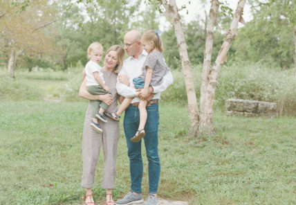 Katherine and Marc Lazar holding their two young children in a park.
