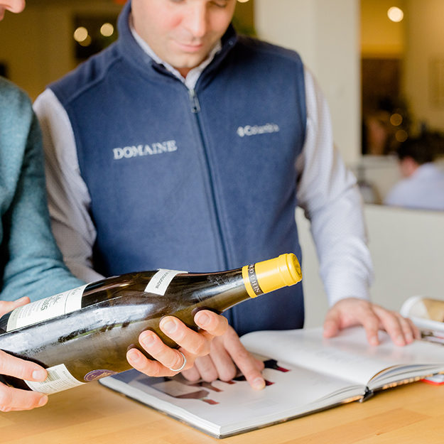 Two Domaine employees examine a bottle and compare it to a catalogue for someone wanting to sell fine wine.