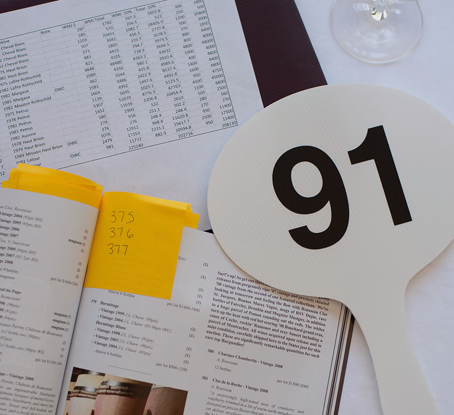 An auction paddle with the number 91 sits on top of auction sheets and catalogues for someone wanting to sell fine wine.