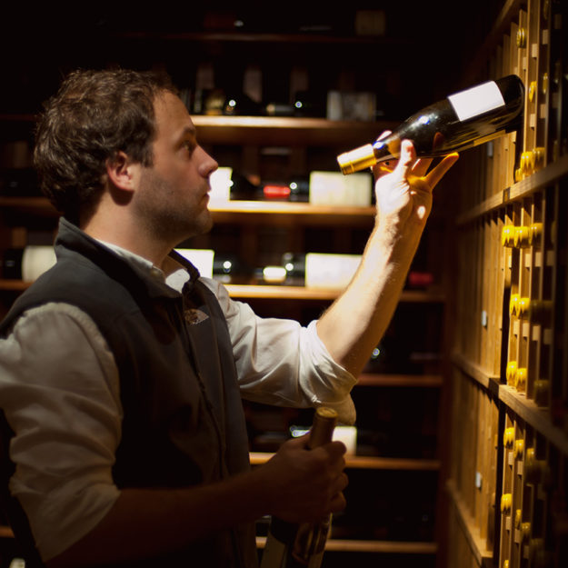 A male Domaine employee puts away a bottle of wine in a home cellar as he aids with wine organization.