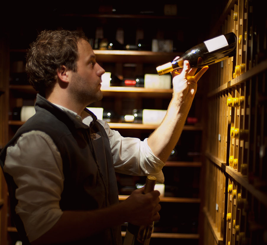 A male Domaine employee puts away a bottle of wine in a home cellar as he aids with wine organization.