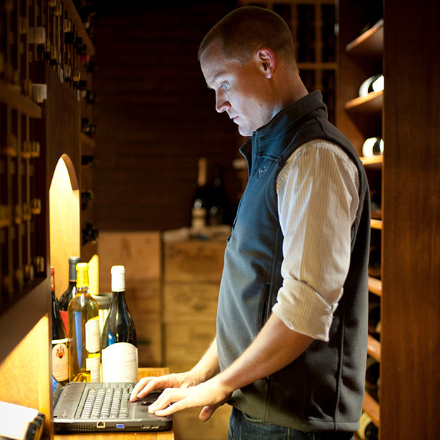 A Domaine employee uses a laptop in a cellar to inventory each bottle of wine, as a part of the wine organization process.