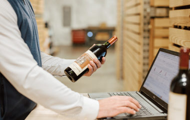 A man using a laptop inventories a bottle of wine for a client that is receiving Domaine cellar management.